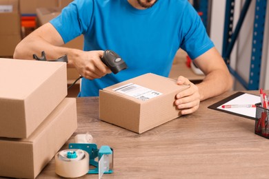 Post office worker with scanner reading parcel barcode at counter indoors, closeup