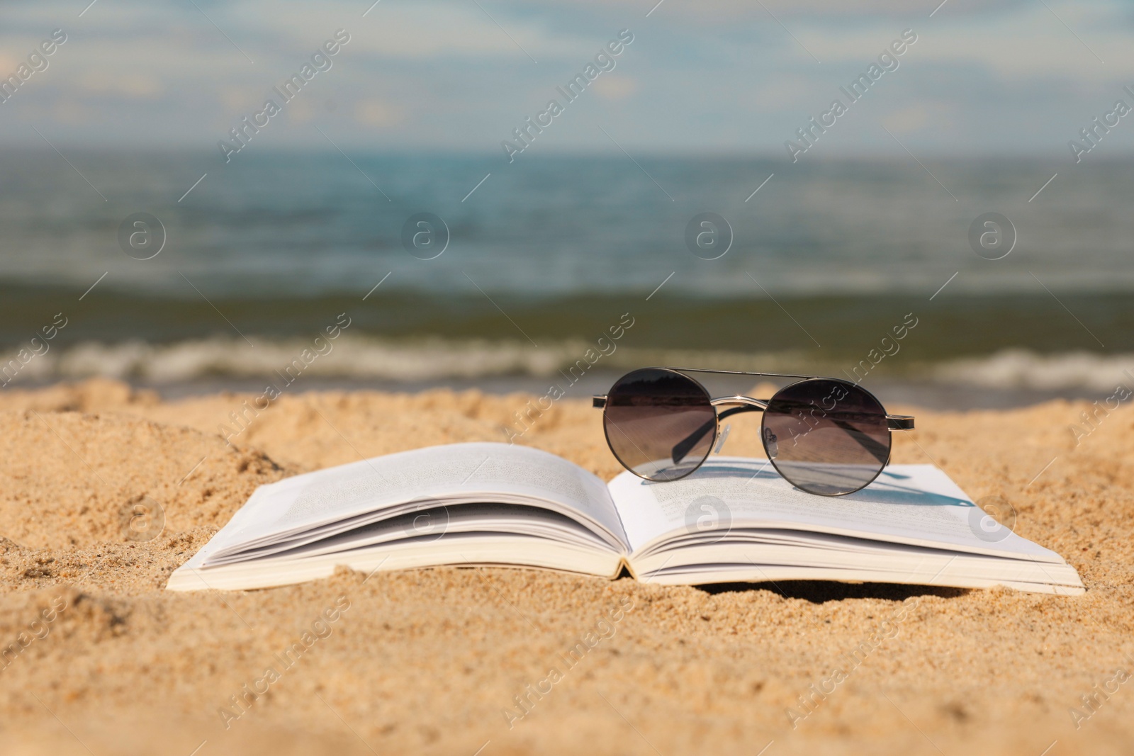 Photo of Open book and sunglasses on sandy beach near sea