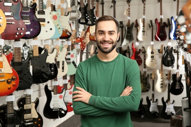 Photo of Young shop assistant near guitars in music store