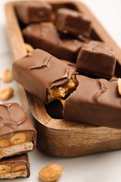 Photo of Wooden board of chocolate bars with caramel, nuts and nougat on white table, closeup