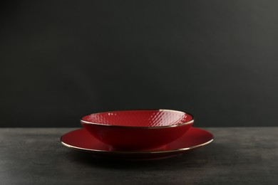 Photo of Red ceramic plate and bowl on gray table against black background, space for text