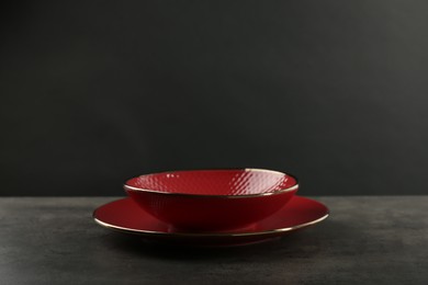 Red ceramic plate and bowl on gray table against black background, space for text