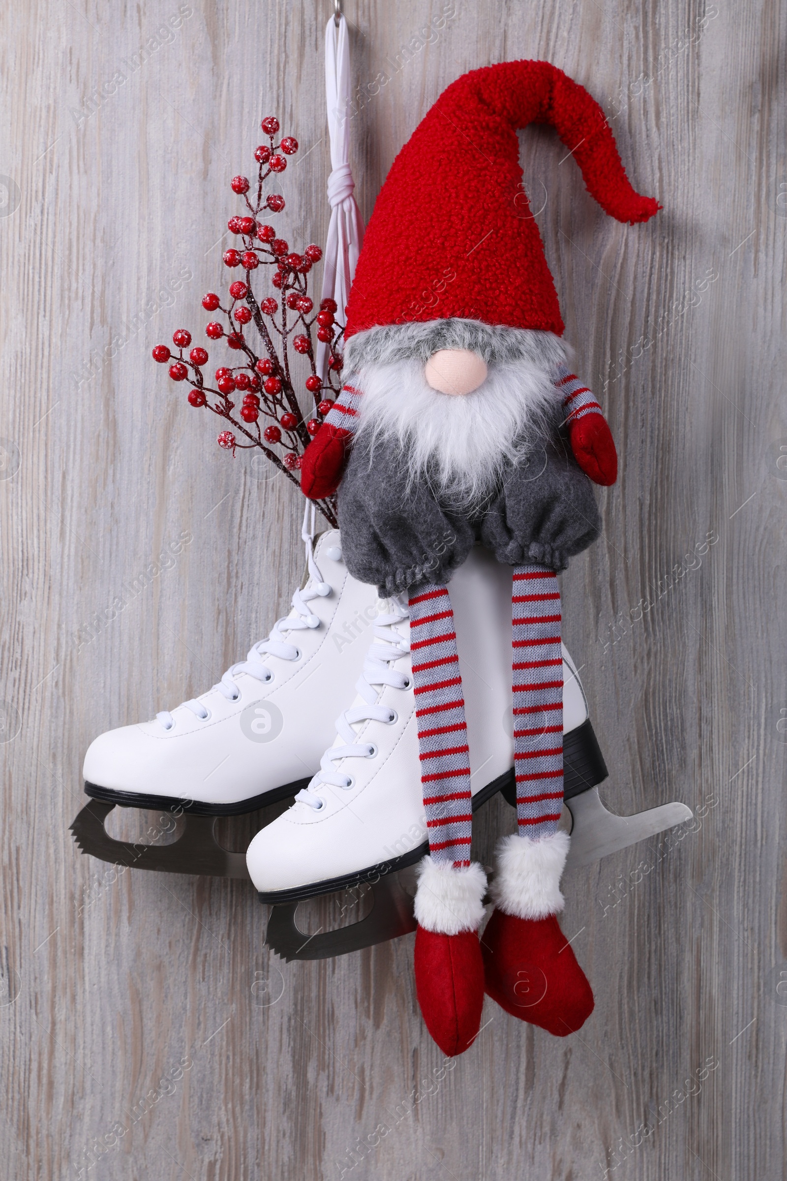 Photo of Pair of ice skates with Christmas gnome and decorative branches hanging on wooden wall