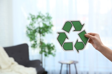 Woman holding recycling symbol on blurred background, closeup. Space for text