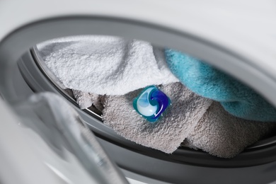 Laundry detergent capsule and towels in washing machine drum, closeup view