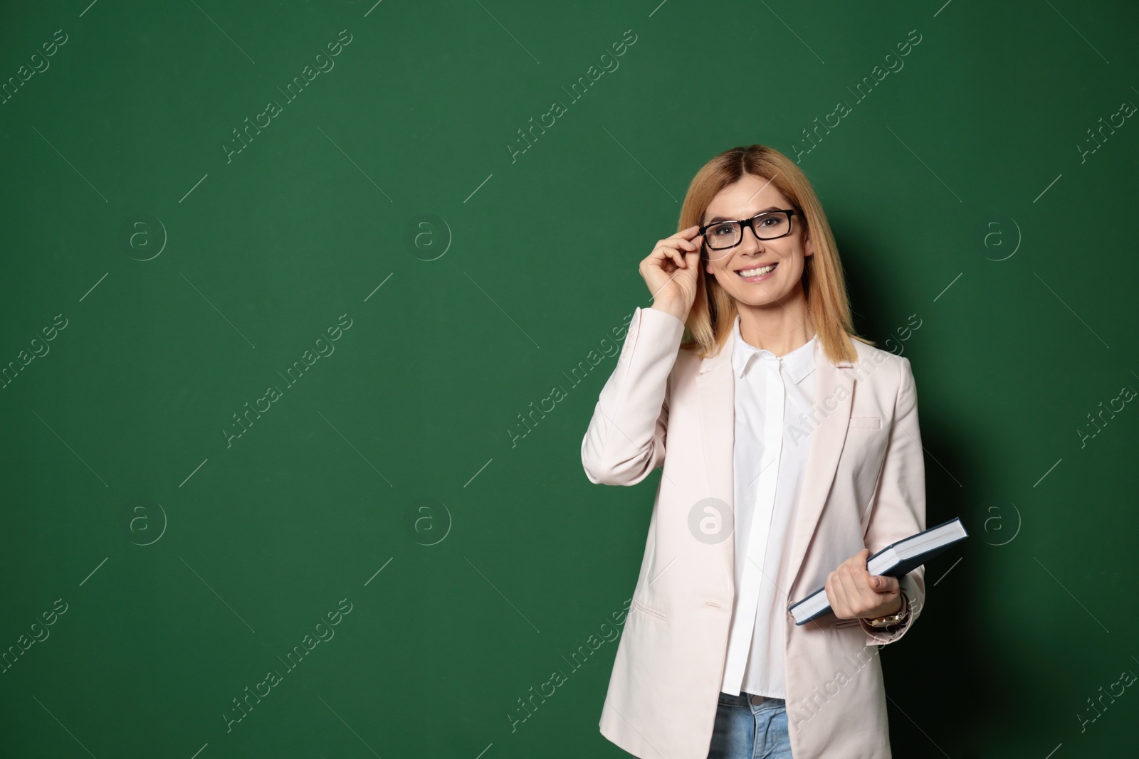 Photo of Portrait of beautiful teacher with book near chalkboard, space for text