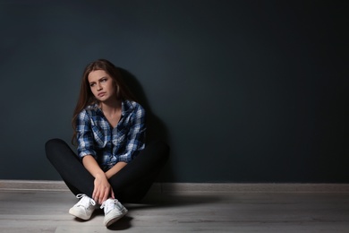 Depressed young woman sitting on floor in darkness