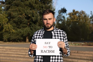 Young man holding sign with phrase Say No To Racism outdoors