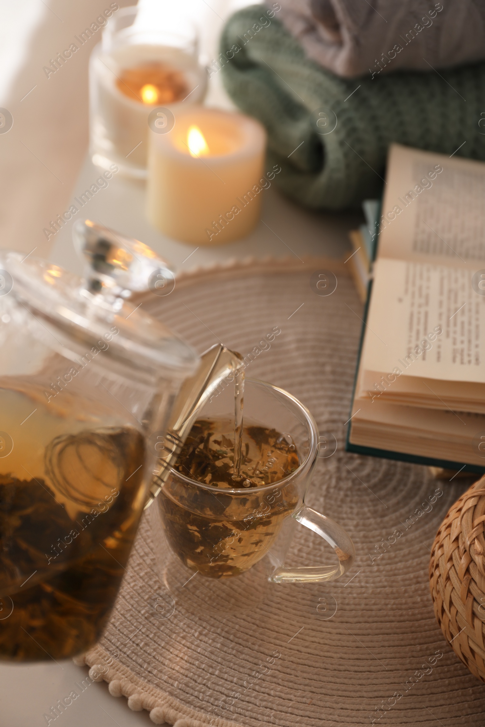 Photo of Pouring freshly brewed tea into cup at table in room, closeup. Cozy home atmosphere