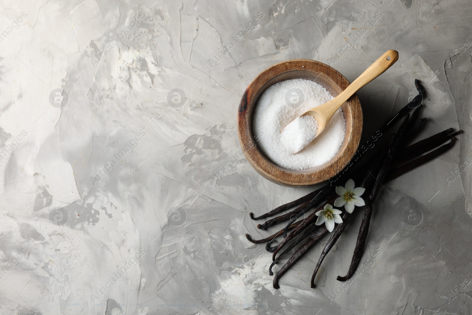 Photo of Sugar in bowl, vanilla pods and flowers on grey textured table, flat lay. Space for text