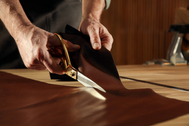 Photo of Man cutting leather with scissors in workshop, closeup