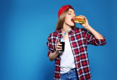 Pretty woman with tasty burger and cola on color background. Space for text