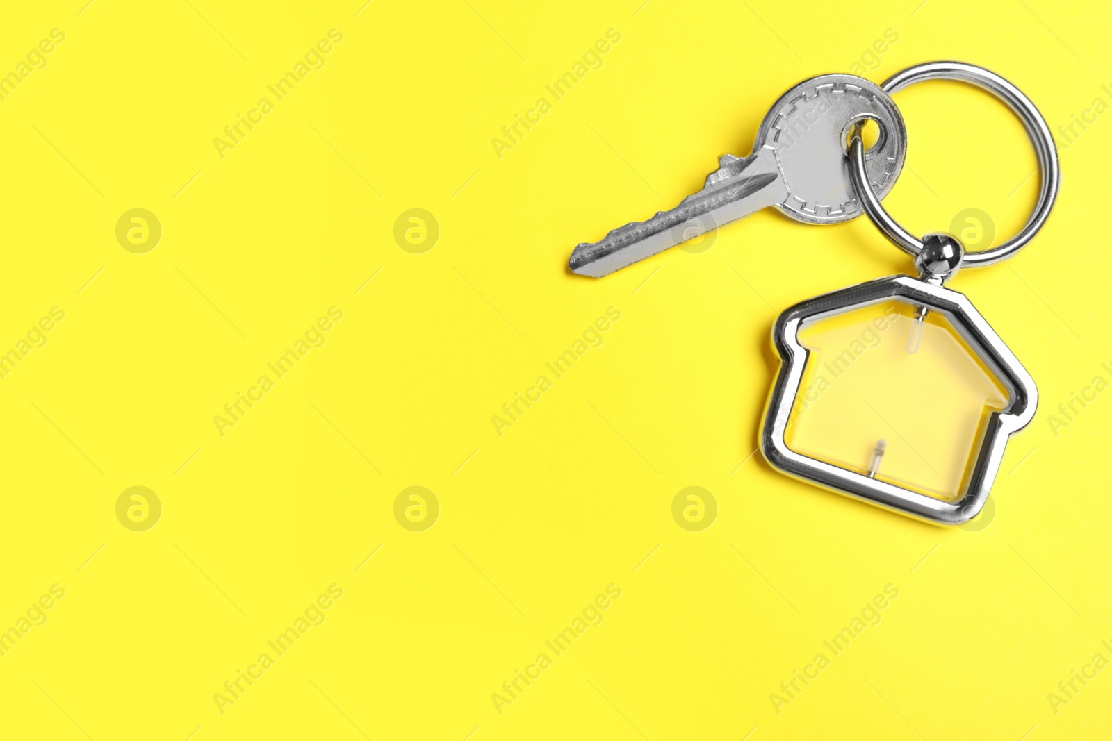 Photo of Key with trinket in shape of house on yellow background, top view and space for text. Real estate agent services