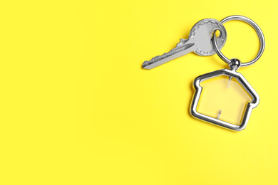 Photo of Key with trinket in shape of house on yellow background, top view and space for text. Real estate agent services
