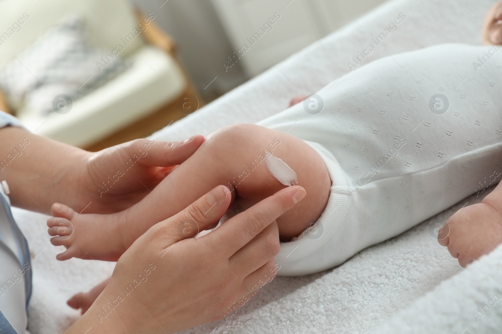 Photo of Mother applying body cream on her little baby indoors, closeup