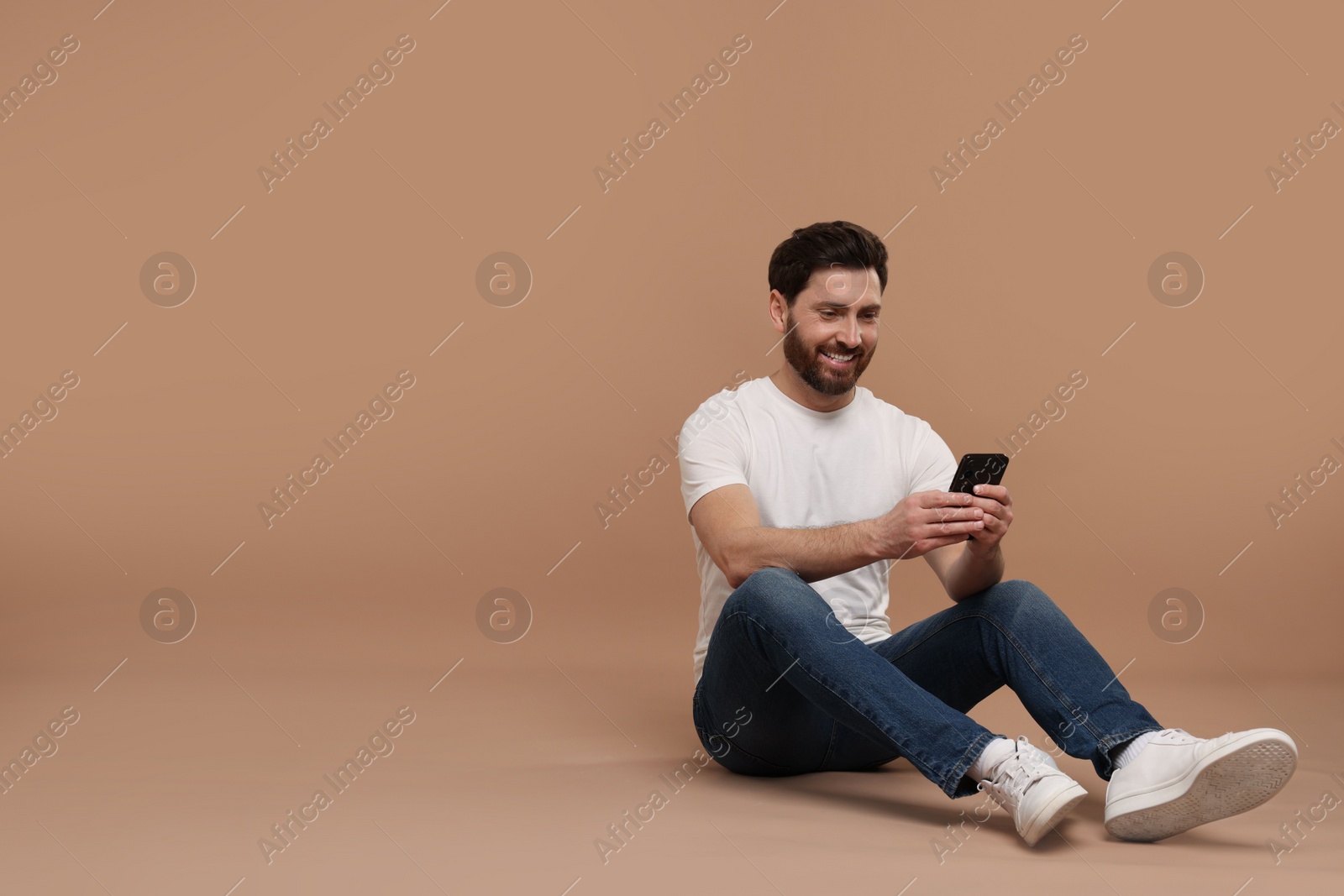 Photo of Smiling man with smartphone on light brown background. Space for text