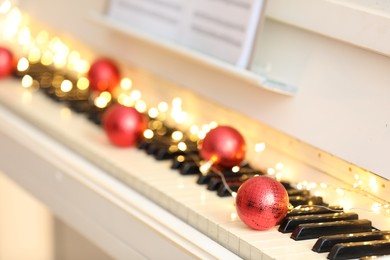 Photo of Red baubles and fairy lights on piano keys, closeup. Christmas music