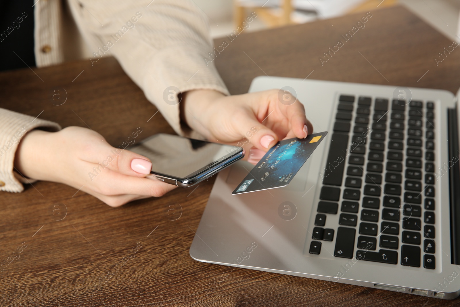 Photo of Online payment. Woman using smartphone and credit card near laptop at wooden table indoors, closeup