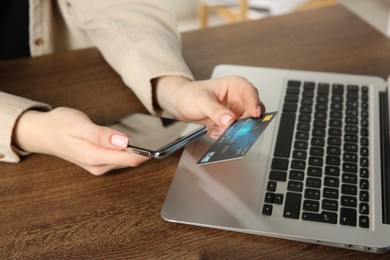 Photo of Online payment. Woman using smartphone and credit card near laptop at wooden table indoors, closeup