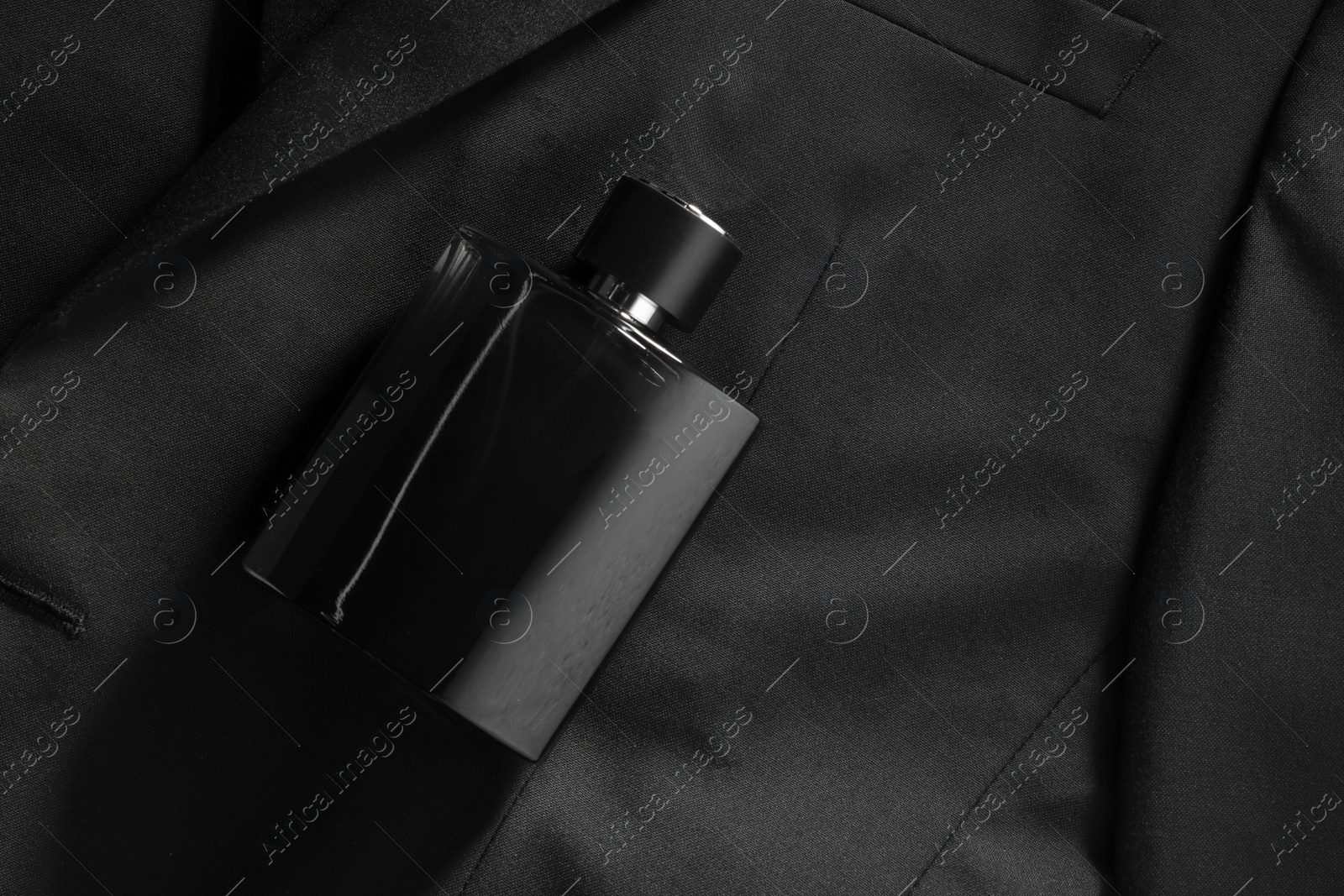 Photo of Luxury men's perfume in bottle on black jacket, top view. Space for text