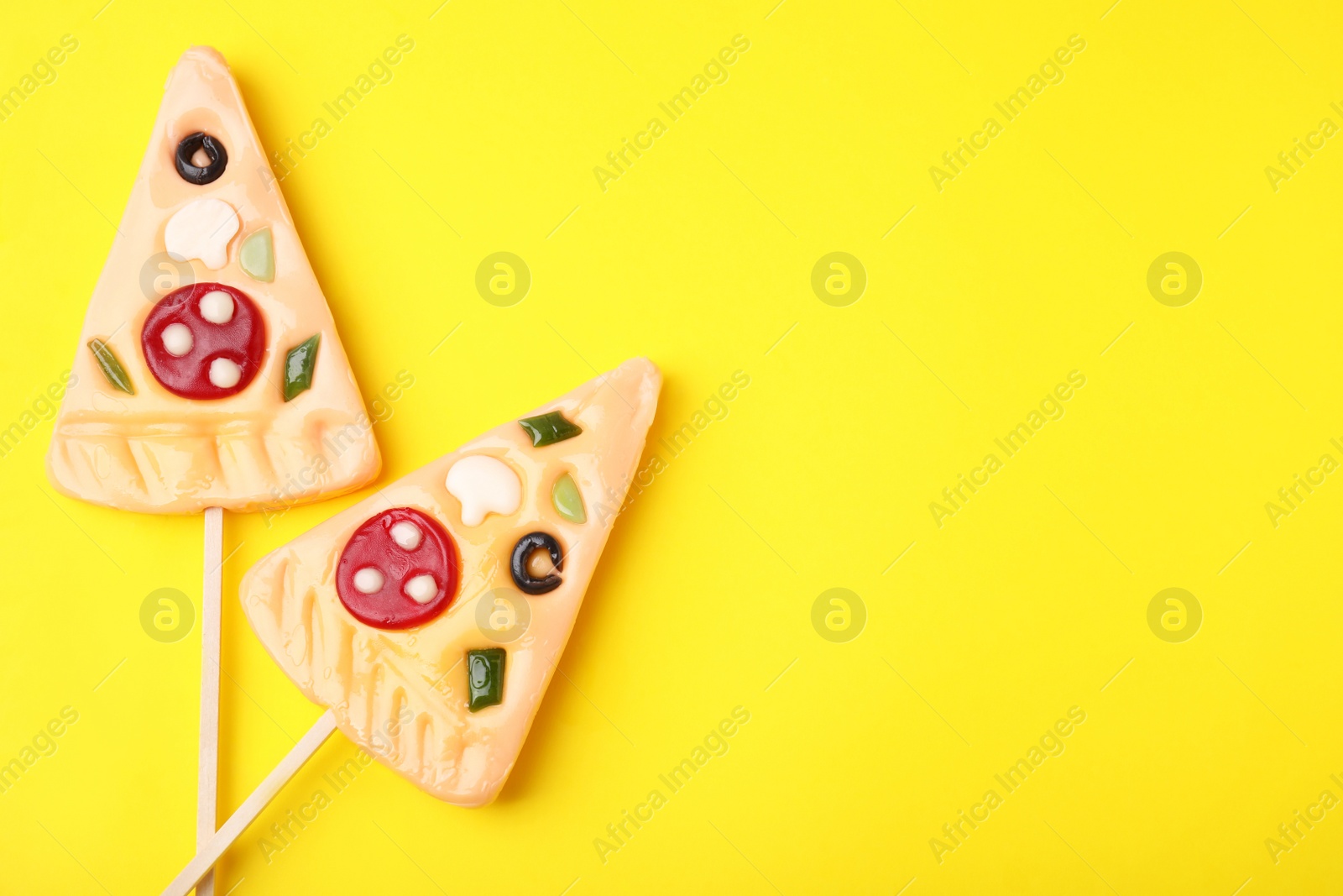 Photo of Pizza shaped lollipops on yellow background, flat lay. Space for text