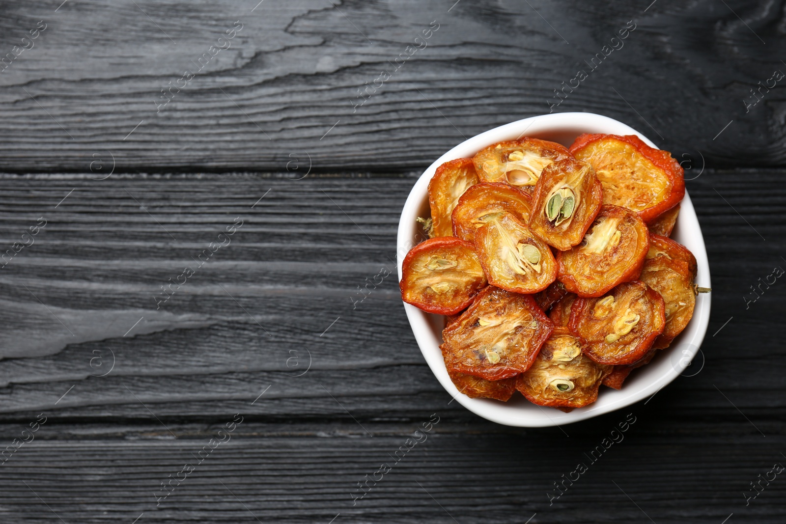 Photo of Bowl with cut dried kumquat fruits on black wooden table, top view. Space for text