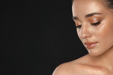 Photo of Beautiful young woman with glitter makeup on black background, space for text