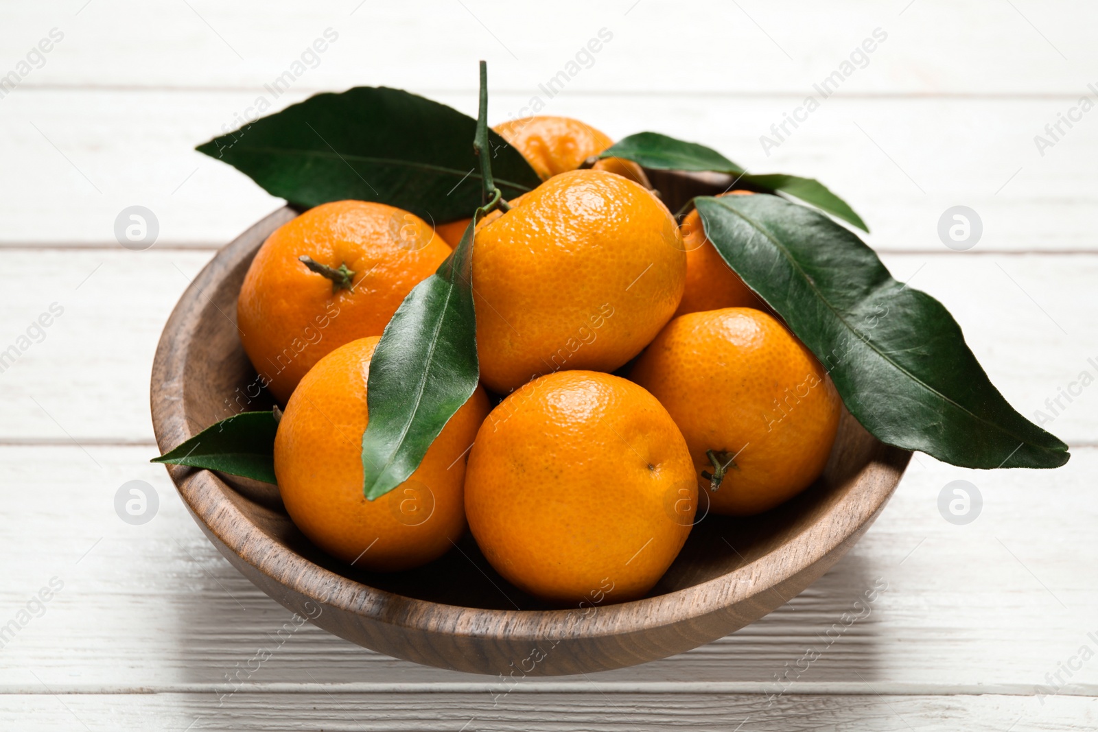 Photo of Fresh ripe tangerines with leaves in bowl on white wooden table. Citrus fruit