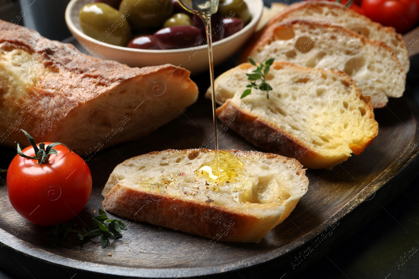 Photo of Pouring oil onto slices of bread on wooden plate, closeup