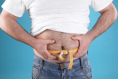 Photo of Overweight man with large belly and measuring tape on color background, closeup