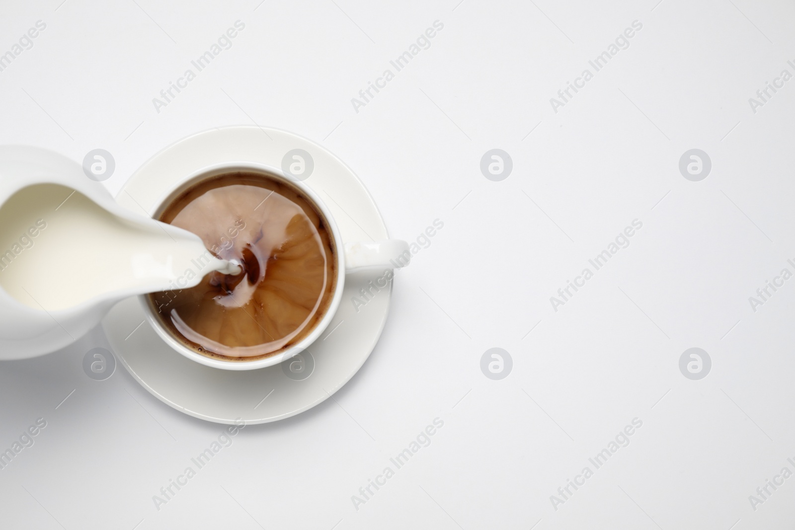 Photo of Pouring milk into cup of coffee on white background, top view