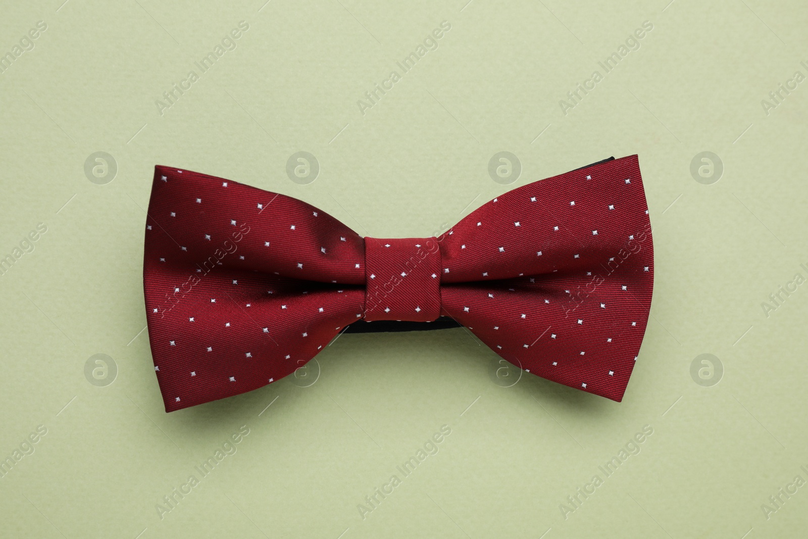 Photo of Stylish burgundy bow tie with polka dot pattern on pale green background, top view