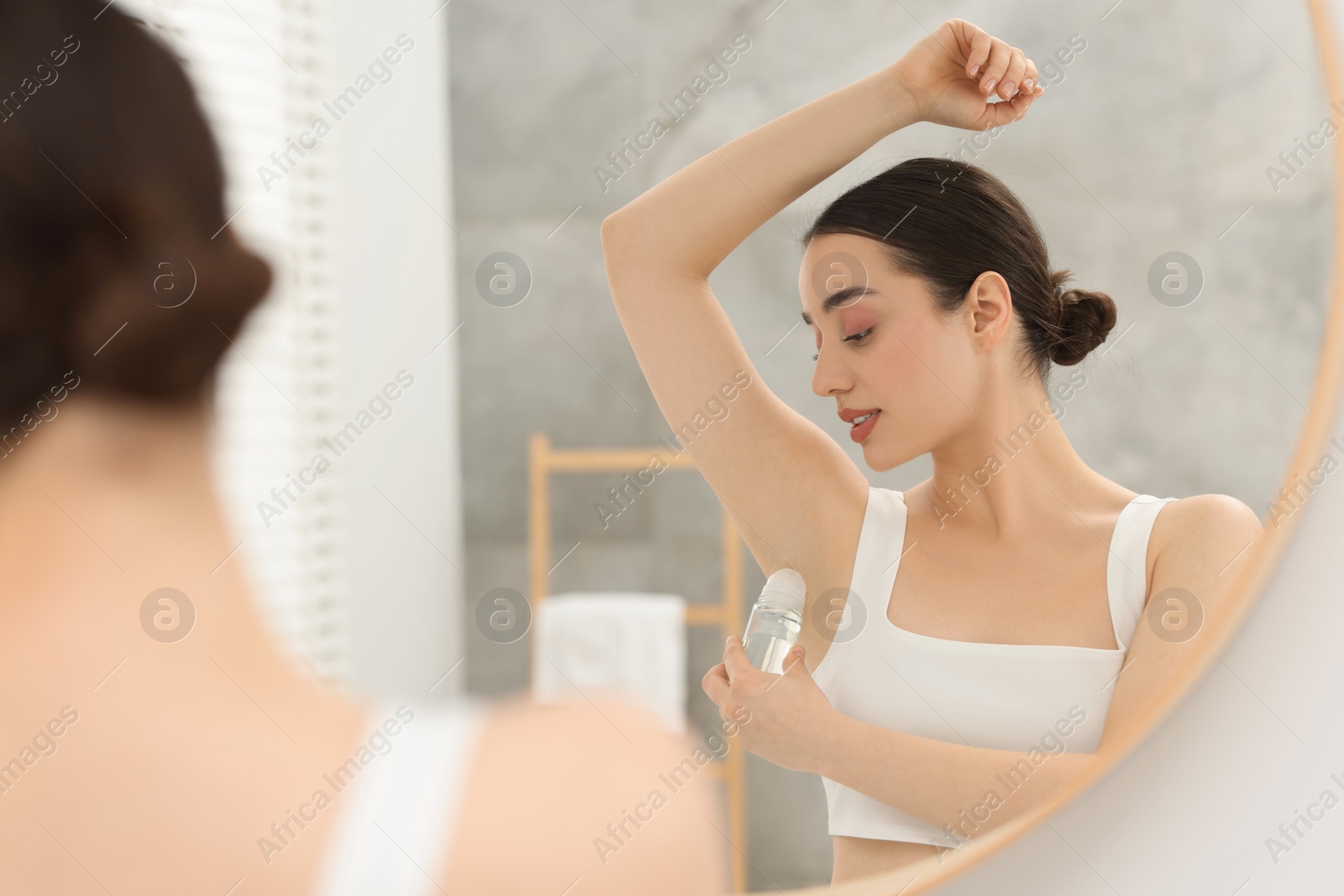 Photo of Beautiful woman applying deodorant near mirror in bathroom