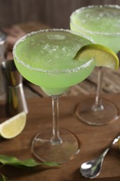 Delicious Margarita cocktail in glasses, lime and bar spoon on table