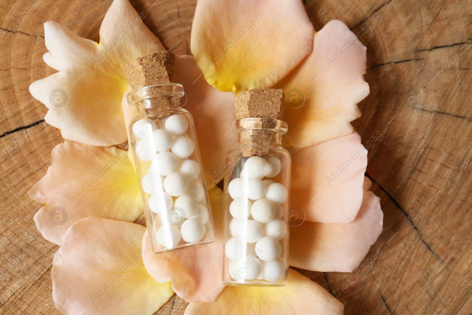 Photo of Bottles of homeopathic remedy and flower petals on wooden background, flat lay