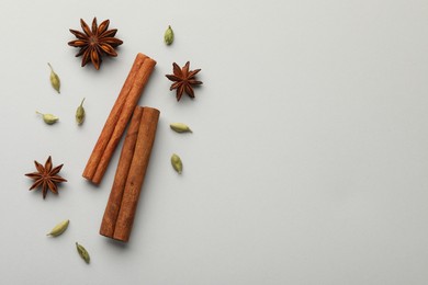 Photo of Cinnamon sticks, star anise and cardamom pods on light grey background, flat lay. Space for text