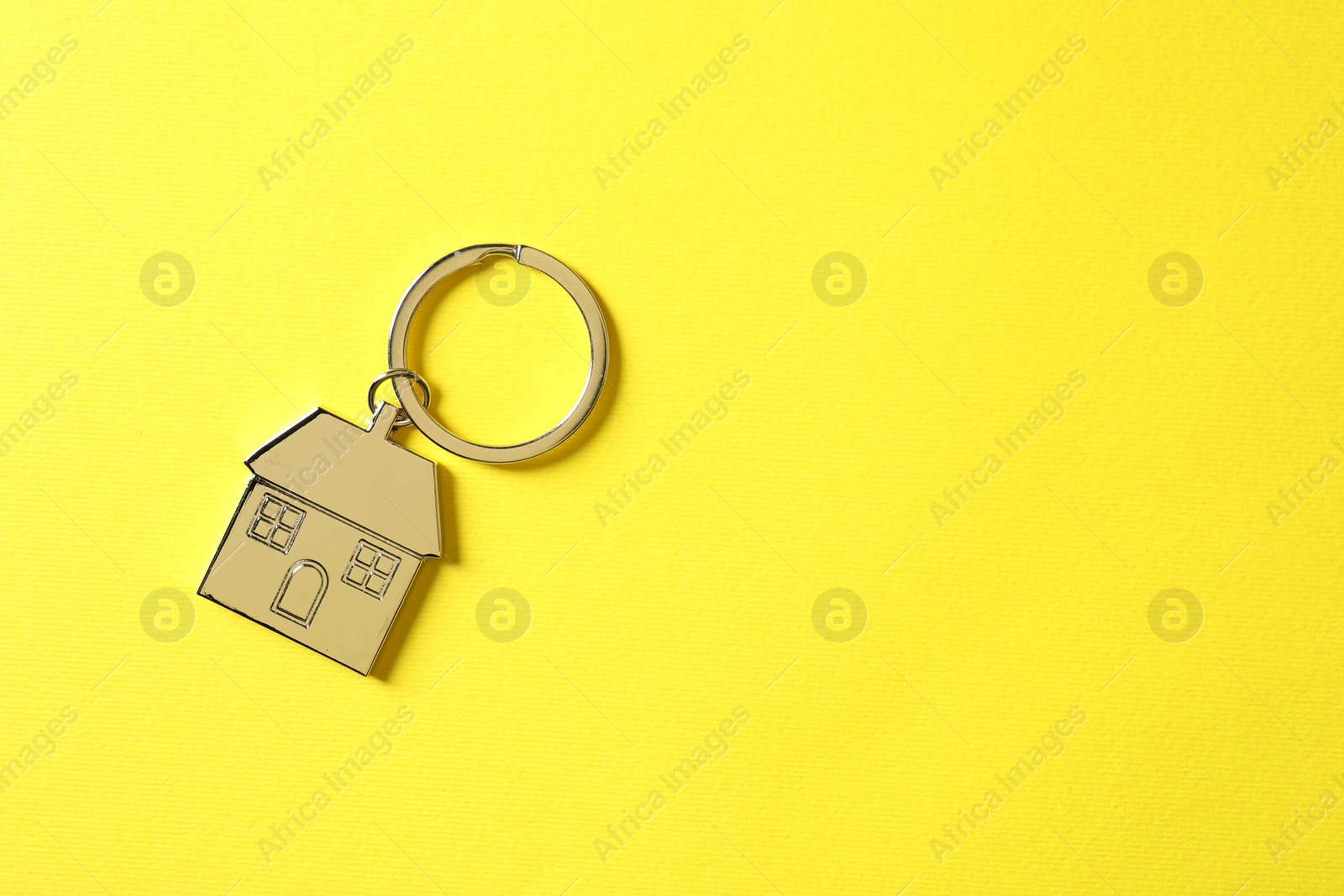 Photo of Metallic keychain in shape of house on yellow background, top view. Space for text