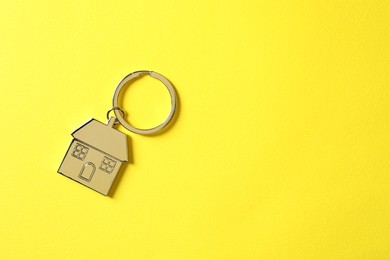 Metallic keychain in shape of house on yellow background, top view. Space for text