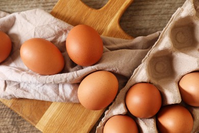 Raw chicken eggs with carton, napkin and board on wooden table, flat lay