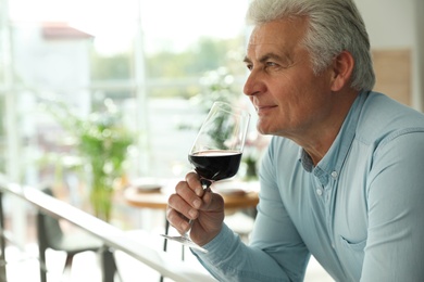 Senior man with glass of wine in restaurant. Space for text