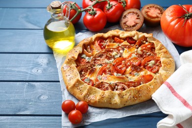 Photo of Tasty galette with tomato and cheese (Caprese galette) on blue wooden table, closeup