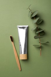 Photo of Bamboo toothbrush and tube of paste on green background, flat lay. Conscious consumption