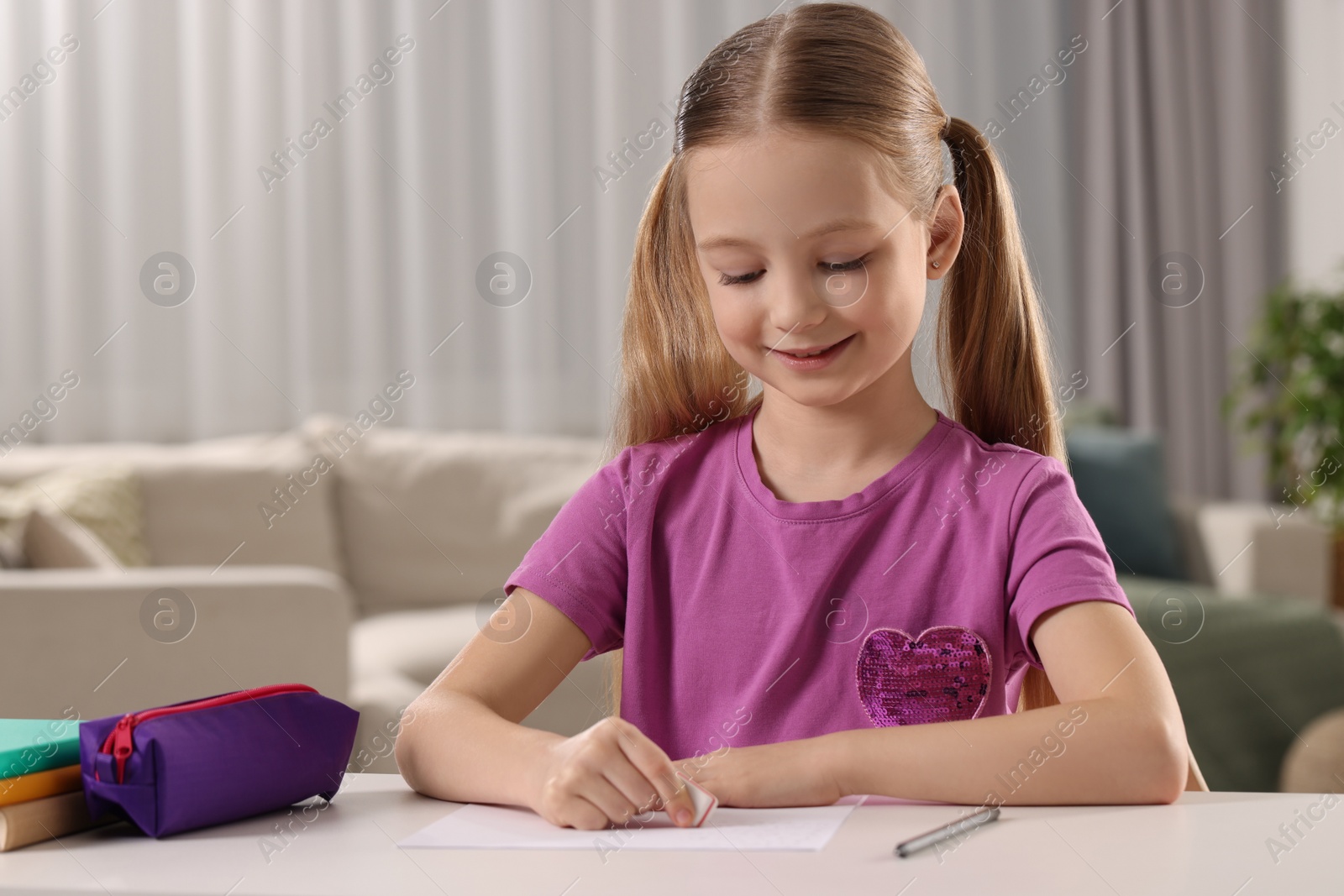 Photo of Girl using eraser at white desk in room