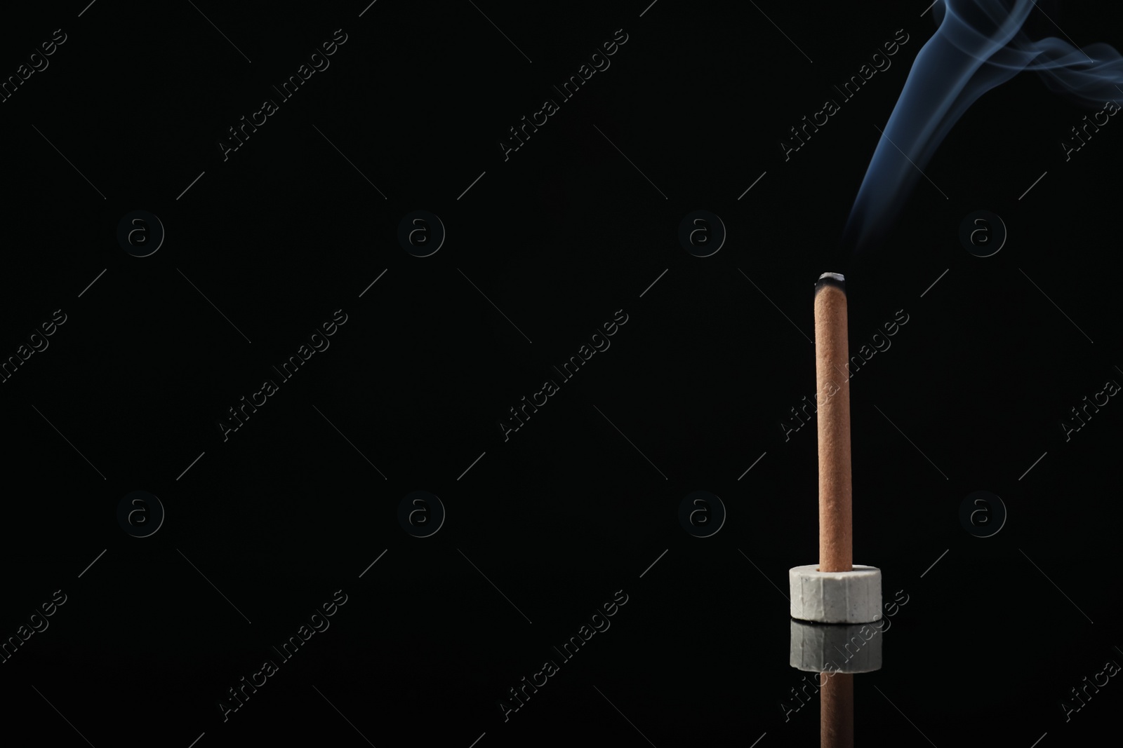 Photo of Incense stick smoldering in holder on black background. Space for text