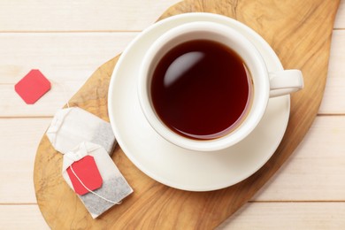 Tea bags and cup of hot beverage on light wooden table, top view