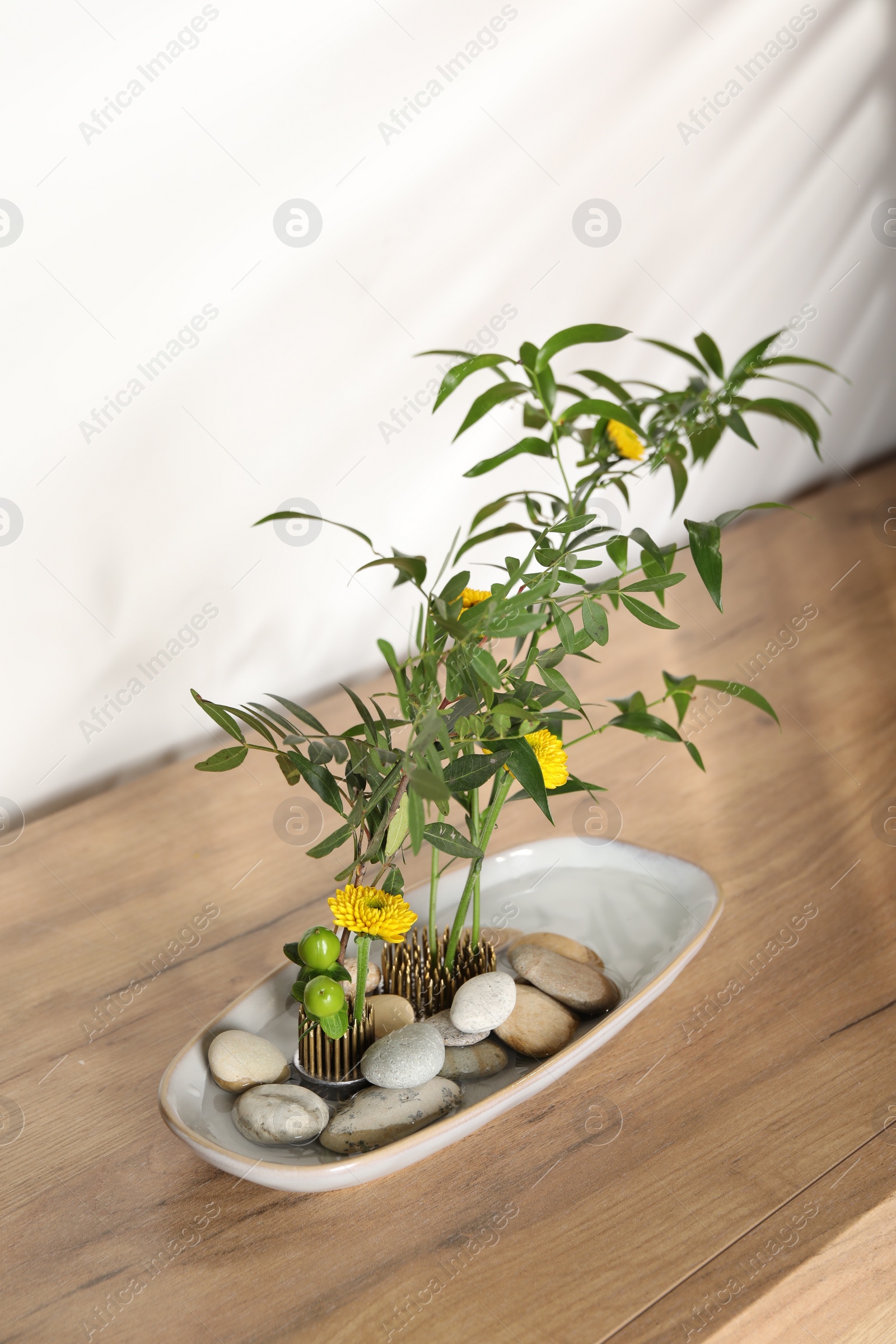 Photo of Ikebana art. Beautiful yellow flowers and green branches on wooden table, above view