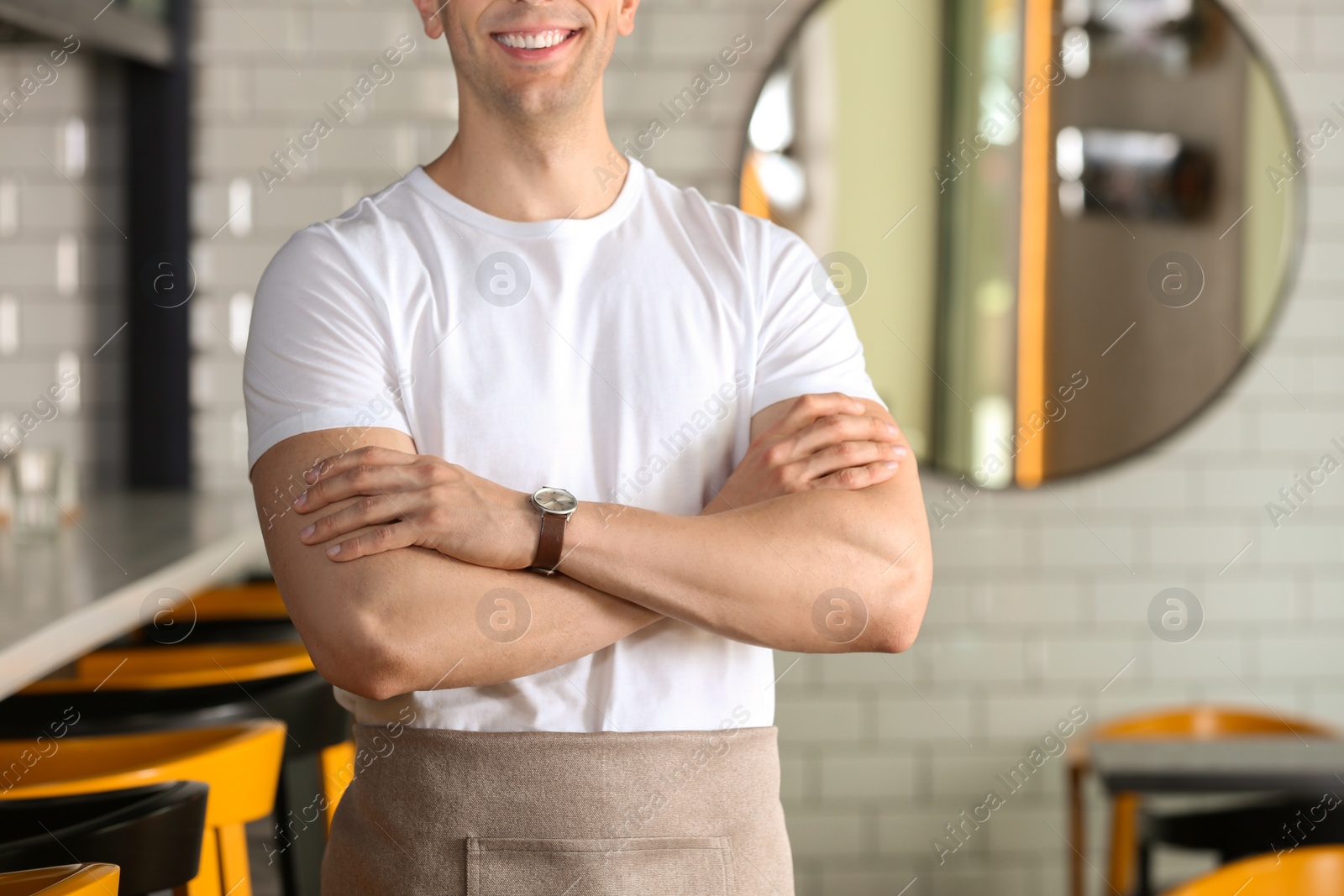 Photo of Young waiter in uniform at cafe