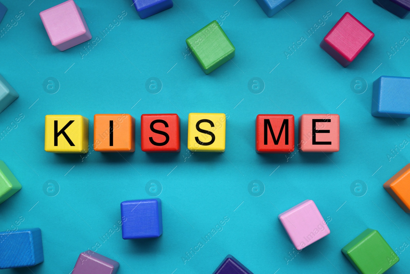 Photo of Colorful cubes with phrase Kiss Me on light blue background, flat lay