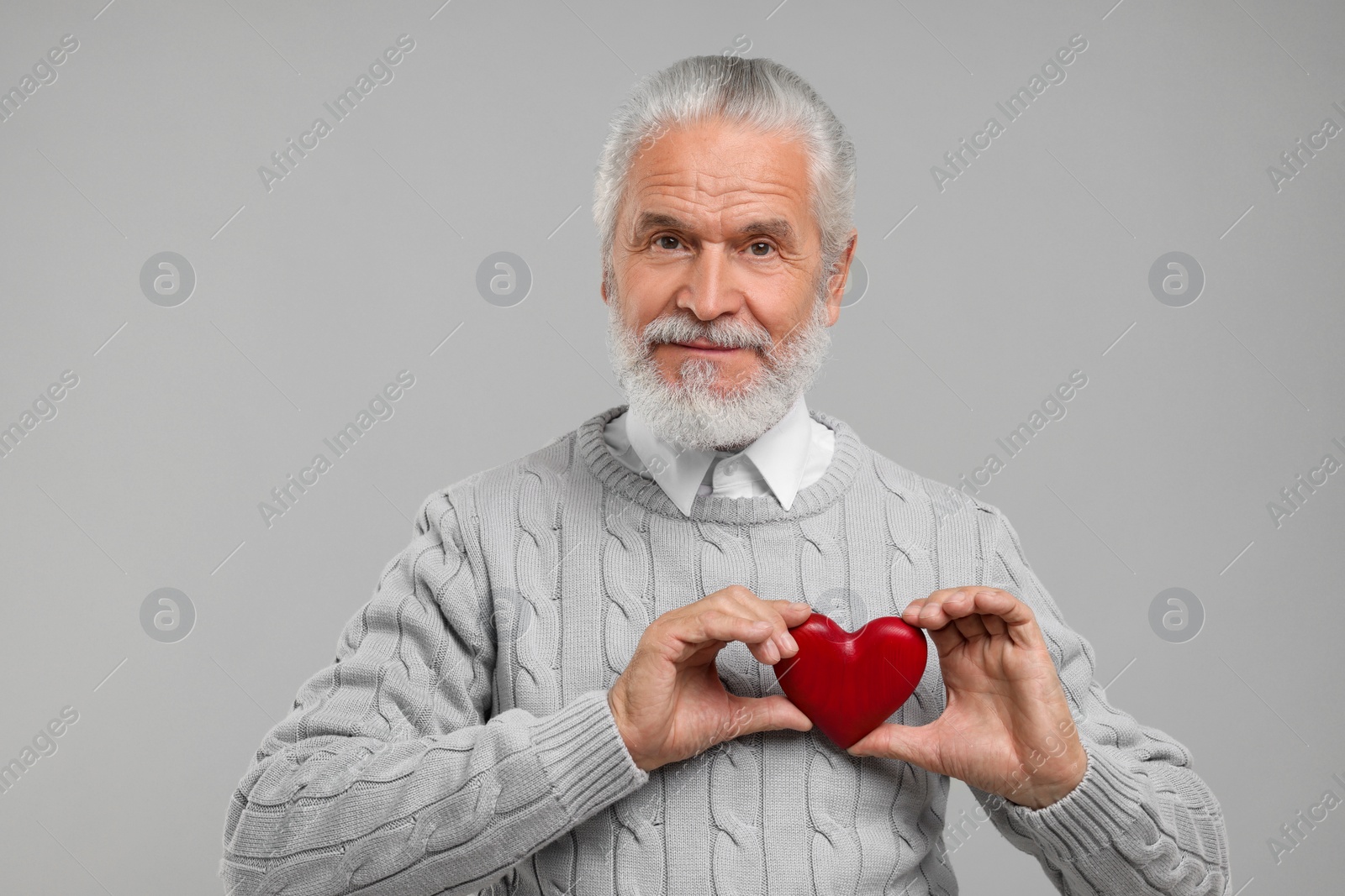 Photo of Senior man with red decorative heart on light grey background