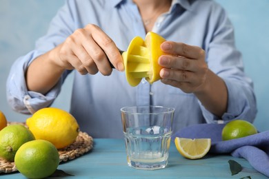 Woman squeezing lemon juice with citrus reamer at light blue wooden table, closeup